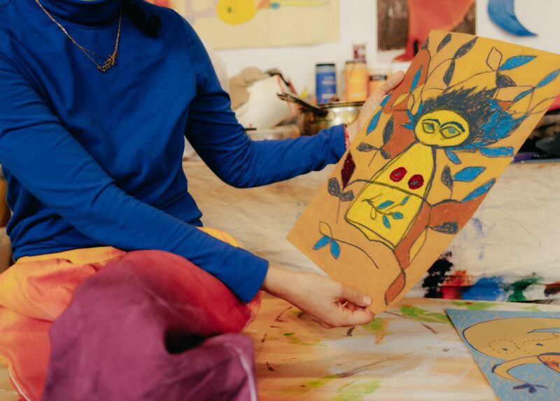 Close up of Tamar Ettun's hands holding up a drawing of a figure on a brown sheet of paper.